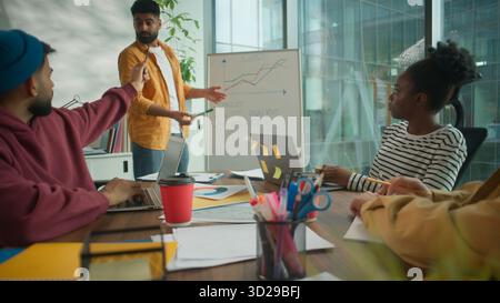 Multicultural informal diversity business team in coworking office listening to male colleague leader presenting financial growth chart on whiteboard Stock Photo