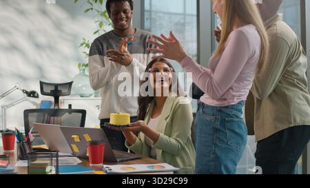 Indian businesswoman Arabian woman working laptop in office three multiracial business colleagues make surprise celebrating congratulate with birthday Stock Photo