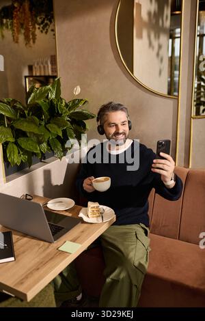 Handsome man in smart attire relaxes in a cafe, enjoying coffee and chatting on his phone. Stock Photo