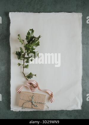 Wrapped present, holly branch, and striped ribbon on textured paper with copy space Stock Photo