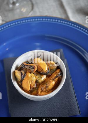 Marinated mussels served as a savory tapa on a rustic white bowl with a blue plate Stock Photo