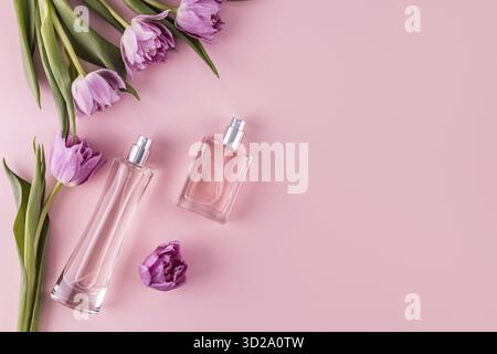 Two stylish glass bottles with perfume on a pink background among spring flowers. A copy space. Top view. Perfume and beauty concept Stock Photo