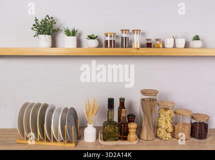 An open kitchen shelf and part of a wooden kitchen countertop with a set of containers for storing food and a dryer with plates. Front view Stock Photo