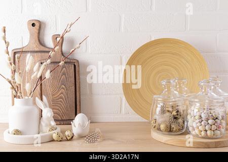 Willow sprigs in a vase, Easter eggs, a rabbit on the kitchen countertop with cutting boards, bamboo dish, jars for bulk products. Easter decor Stock Photo