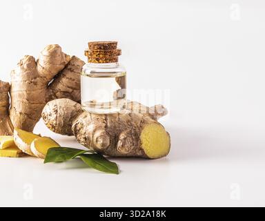 Glass bottle with cork cap with natural ginger root oil stands on a large fresh plant root on a white background. Front view. packaging Stock Photo
