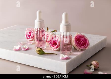 Natural rose petal oil or oil-based serum in two cosmetic bottles on a white marble podium. natural cosmetics. care Stock Photo