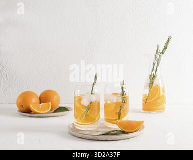 Two glasses in the shape of a jar with orange vitamin water and ice cubes on a white ceramic tray. detox water Stock Photo
