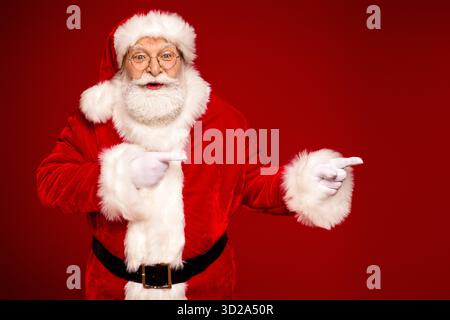 Santa Claus in red suit with white fur points playfully against a bold red background for a festive holiday season image Stock Photo