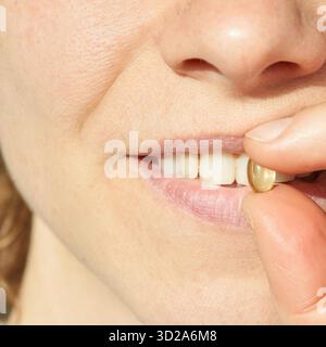 Close-up of young caucasian female holding vitamin capsule near lips in sunlight. || Model released Stock Photo