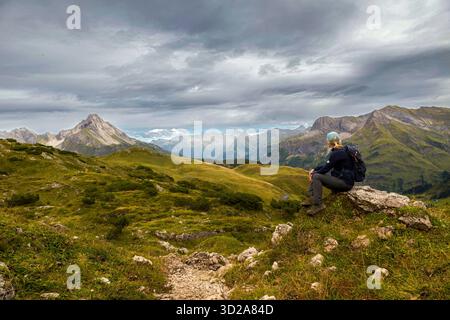 A hiker sits on a hill overlooking a mountainous landscape under grey sky, skirts, Austria, Europe || Model released Stock Photo