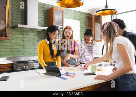 In school, teenagers collaborating on creative project using tablet and photos. Collaboration, teamwork, creativity, technology, innovation, digital || Model released Stock Photo