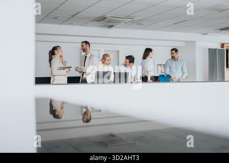 Group of colleagues on a modern office balcony discussing plans with laptops and teamwork in a bright, open space Stock Photo