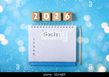 New 2026 Year Goals. Inscription in notebook and cubes with numbers on light blue background, top view. Bokeh lights Stock Photo