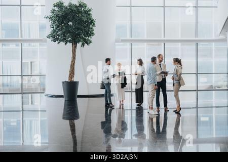 Professional group of colleagues in a modern corporate lobby discussing projects and sharing documents Stock Photo