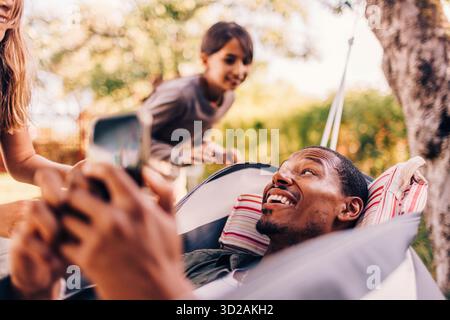 Daughters playing with father lying on hammock Stock Photo