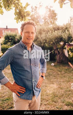 Portrait of smiling man standing with arms akimbo in back yard Stock Photo