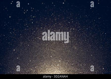 Dark glitter texture with cold shadows illuminated from below, revealing abstract surface with glowing sparkles and shimmering highlights across frame Stock Photo