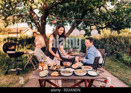 Smiling woman serving herself from food table in back yard at social gathering party Stock Photo