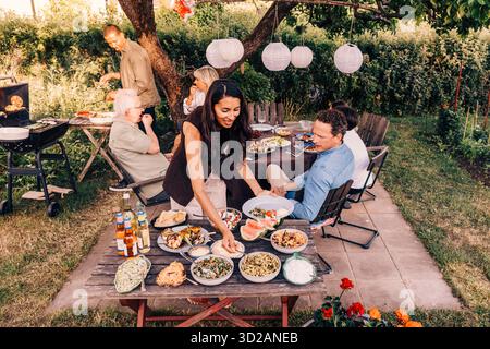 High angle view of smiling woman serving herself from food table in back yard at social gathering party Stock Photo