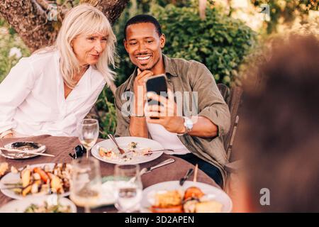 Smiling man taking selfie with mother while sitting at dining table in back yard Stock Photo