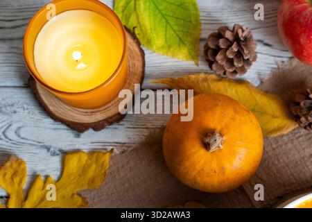Warm autumn composition with candle, pumpkin, pinecones, apple, and colorful leaves on rustic wooden background. Perfect for fall, Thanksgiving, and s Stock Photo