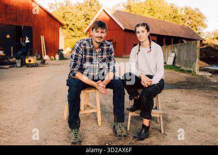 Portrait of male and female farm workers sitting on stools at farm Stock Photo