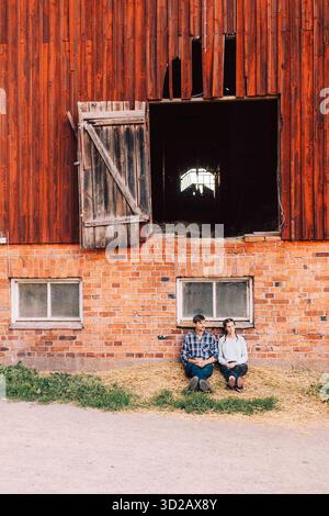 Male and female farm workers sitting by brick wall outside barn Stock Photo