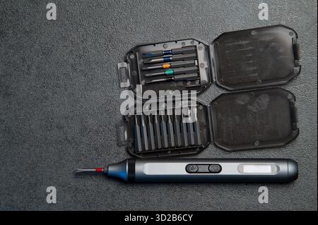 Electric rechargeable cordless mini screwdriver and set of different interchangeable bits in plastic case on a gray background. Stock Photo