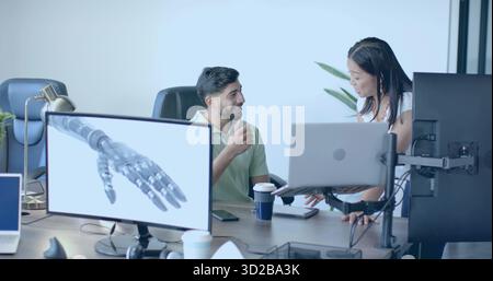 Discussing with team wearing green polo, white blouse on office laptops, with robotic hand monitors Stock Photo