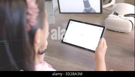 Interacting Asian woman using tablet at home office desk, with VR headset, laptop, copy space Stock Photo