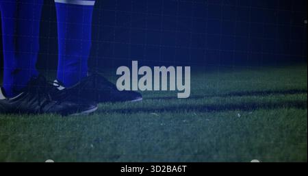 Displaying feet of soccer player standing on night turf, with blue socks, black cleats, copy space Stock Photo