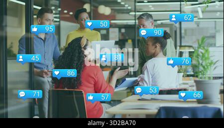 Collaborating five professionals using laptop around table in office under floating digital icons Stock Photo