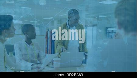 Leaning Black designer in mustard jacket guiding team at design studio table, with laptop, swatches Stock Photo