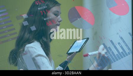 Business analyst writing chart on glass-board in meeting room, with tablet, red marker, copy space Stock Photo