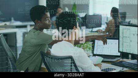 Two adult women collaborating in office, pointing at blueprint on monitor with laptops coffee cup Stock Photo