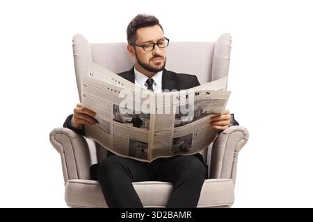 Man in a black suit sitting in an armchair reading a newspaper isolated on white background Stock Photo