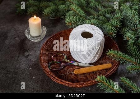Close-up of colorful embroidery scissors and a crochet hook in a spool of white cotton thread on a dark stone background. Handicraft, crochet, and DIY Stock Photo