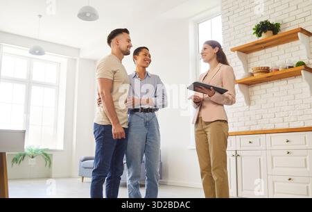 Real-estate agent and young married couple standing in modern domestic kitchen Stock Photo