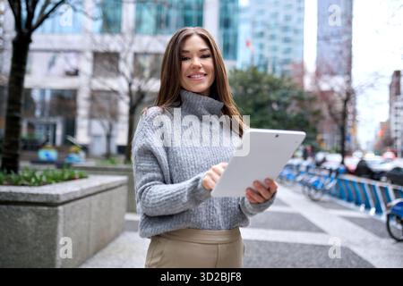 Young happy busy business woman standing in city using digital tablet. Stock Photo