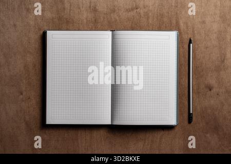 Open notebook with checkered sheets and pencil on wooden texture background, close up, top view, copy space Stock Photo