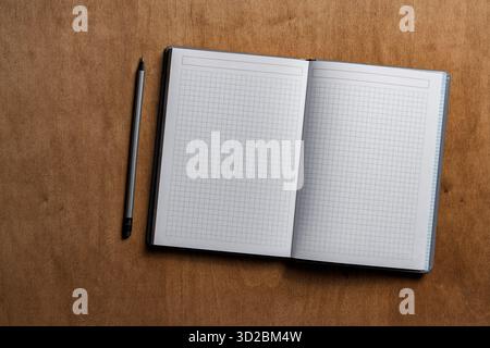 Open notebook with checkered sheets and pencil on wooden texture background, close up, top view, copy space Stock Photo