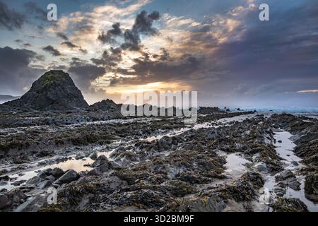 Sun sets behind Black Rock on Widemouth Bay beach Cornwall Stock Photo