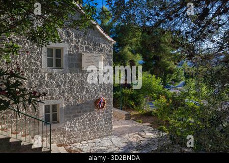 NECUJAM, CROATIA, 09.01.2025:A stone building features a commemorative plaque on the wall, with a wreath tied in red, white, and blue ribbons. Sunlit Stock Photo