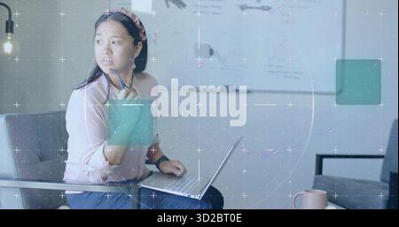 Thinking woman wearing pink blouse holding pen at office area with laptop, mug, copy space Stock Photo