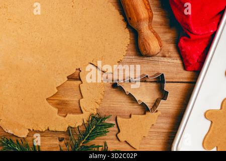 A festive baking scene with rolled-out cookie dough, a Christmas tree cutter, and a rolling pin on a wooden table. Stock Photo