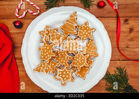A collection of iced gingerbread cookies in various holiday shapes sits on a white plate on a wooden table. Stock Photo