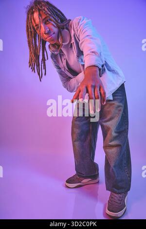 Young man with dreadlocks and headphones reaching arm out in purple neon light Stock Photo