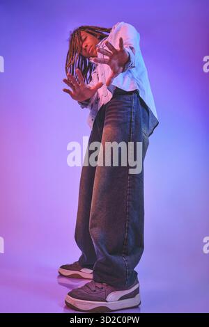 Young man with dreadlocks dancing in baggy jeans under vibrant neon lights Stock Photo