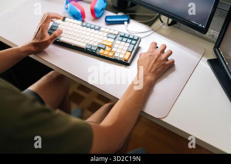 Close-up of unrecognizable remote programmer focusing on coding project, utilizing dual-screen workspace with mechanical keyboard, seated in ergonomic Stock Photo