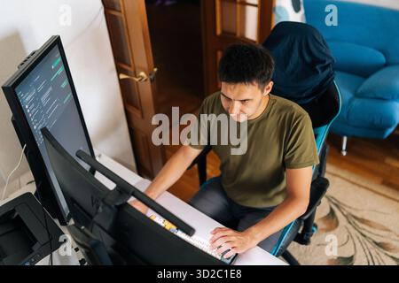 Top view of programmer male working from home office using multiple monitors setup and typing on mechanical keyboard looking to screen while sitting Stock Photo
